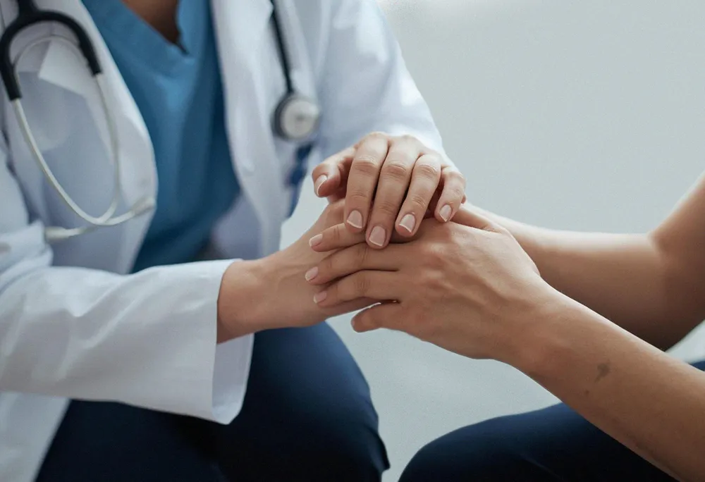 Doctor in scrubs holding a patient's hands during a compassionate consultation